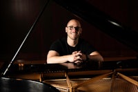 a man with glasses sitting at a piano